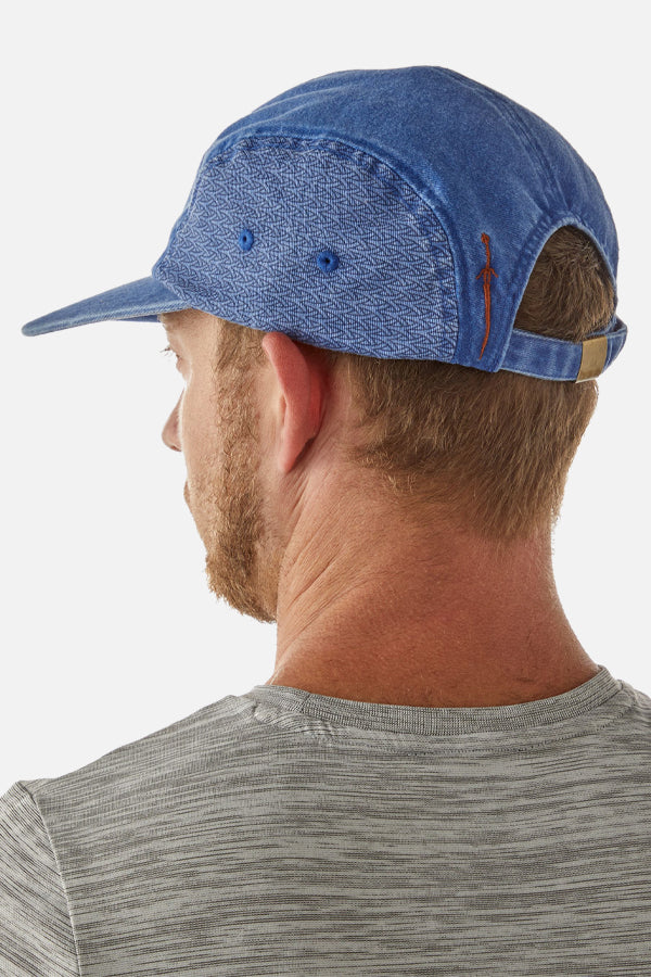 We see an upper profile of a male model from behind, looking to the left. The man has a light blond beard and short blond hair, wearing a white striped shirt. He sports a blue denim-styled cap with a pattern on the left side, and at the back of his head, we can see the adjustable strap.